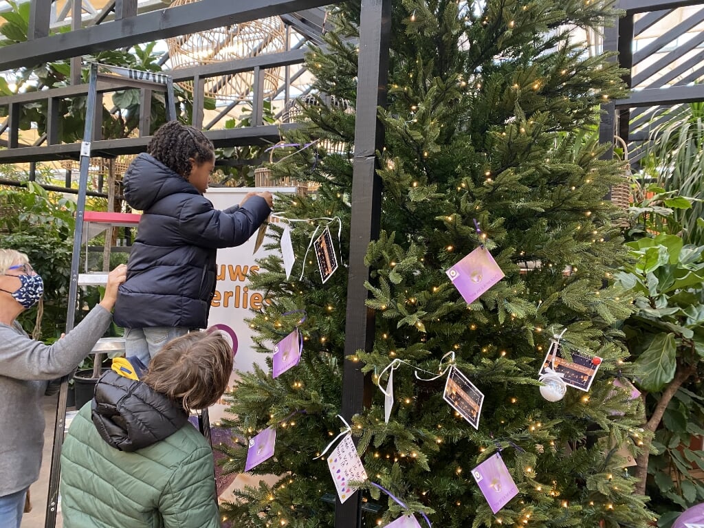 Kinderen hangen een wens in de kerstwensboom.