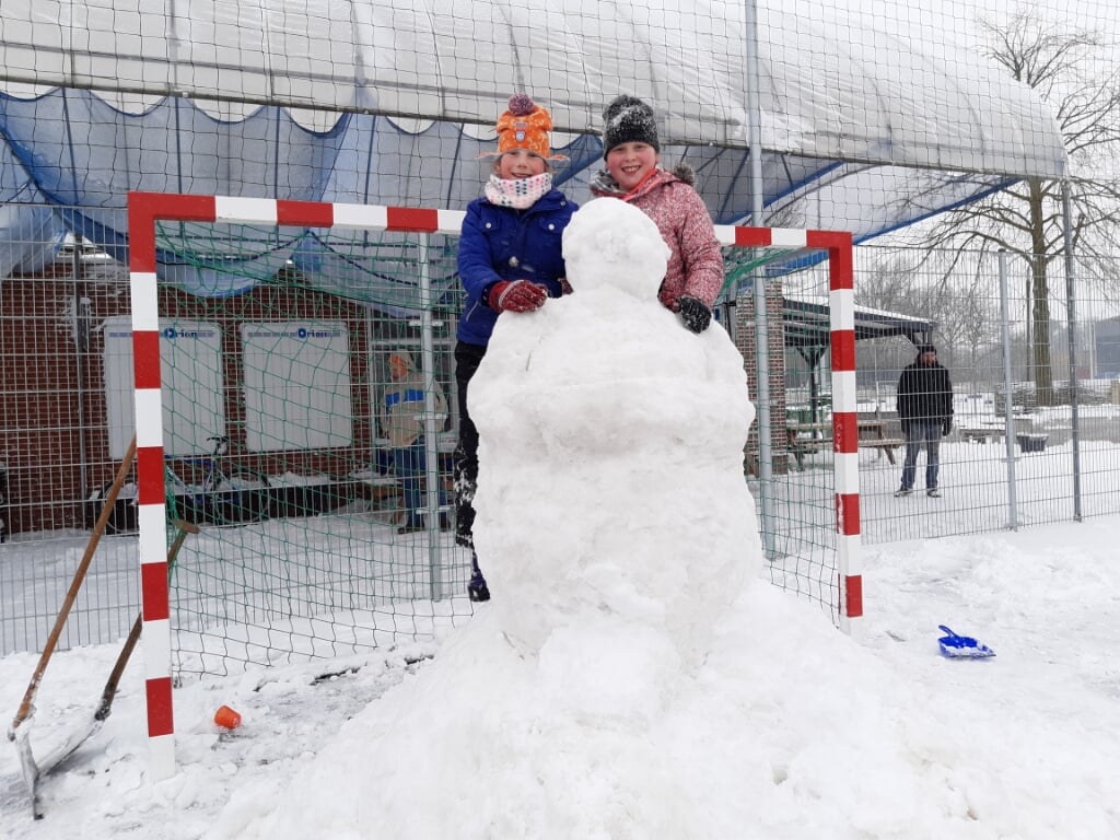 Twee trotse sneeuwpopbouwers poseren voor de zojuist gemaakte sneeuwkeeper