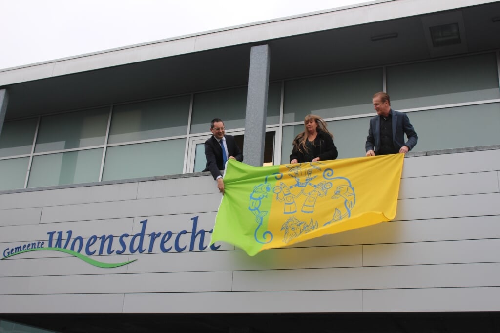 Burgemeester Adriaansen, Petra van Eekelen en wethouder Hans de Waal tonen de vlag vanaf het bordes bij het gemeentehuis.