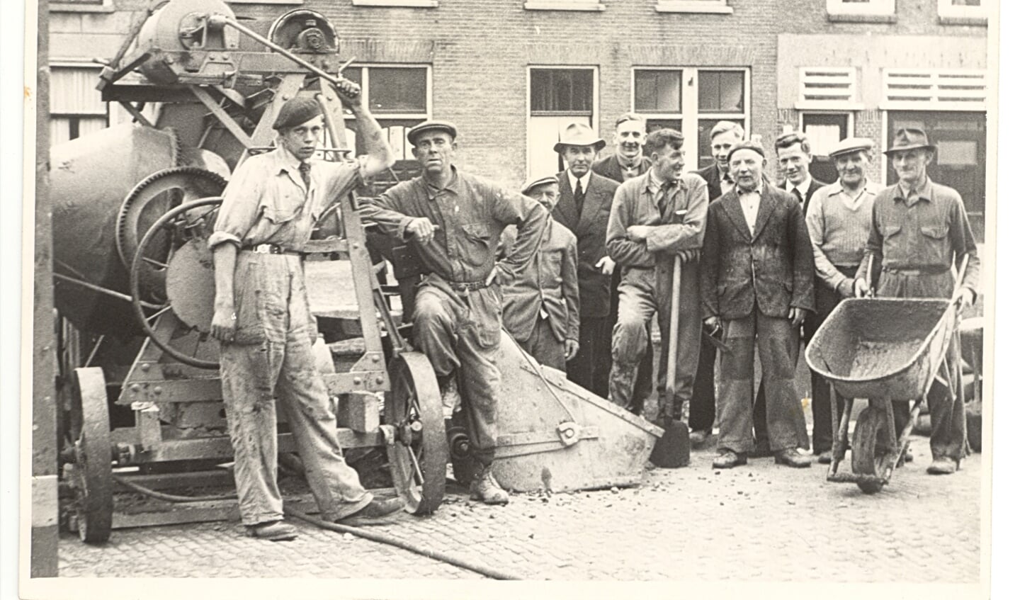Bijschrift: Een fraaie foto van het personeel van Mensert aan het Achterom in 1955, toen de mannen nog van staal waren en mensen uit de ramen hingen als een foto werd gemaakt.