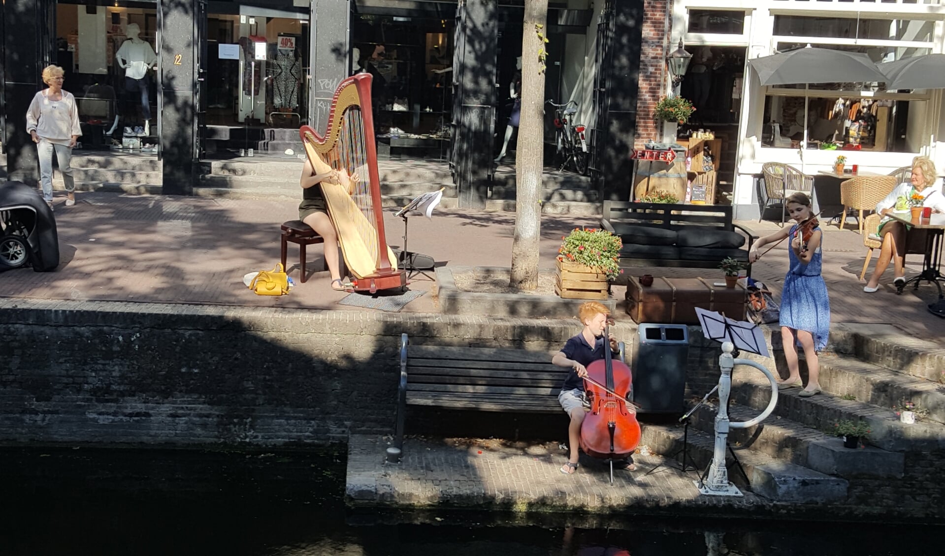 Het DOC-trio, Douwe (cello), Dominique (harp) en Claire (viool), musiceert langs de gracht in de binnenstad. 