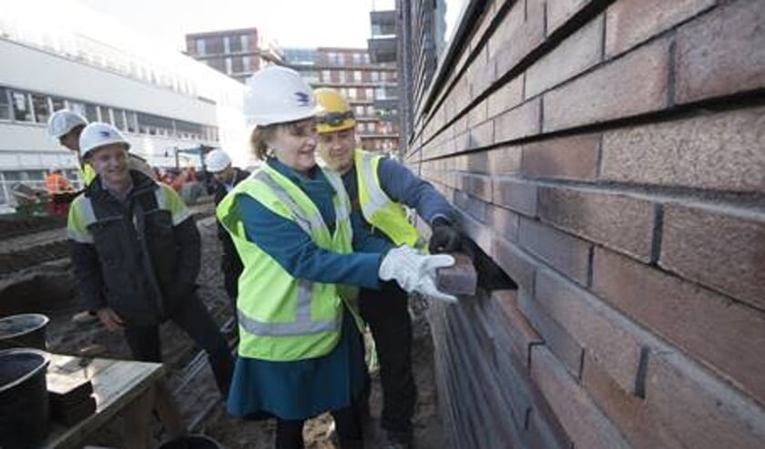 Wethouder Martina Huijsmans metselt de laatste steen in de buitenkant van het woningproject VOLT in.