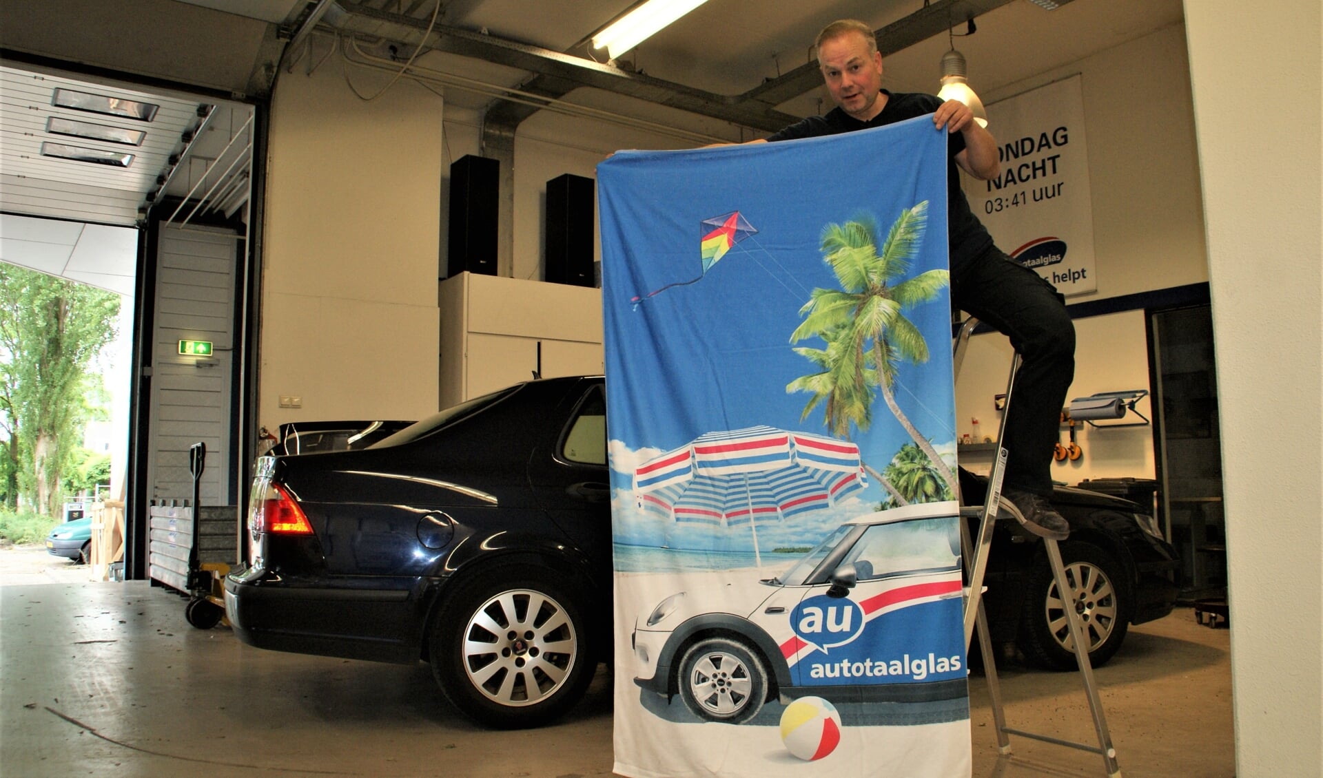 Rob Struik toont het Autotaalglas badlaken, als cadeau bij een complete ruitvervanging bij de auto.