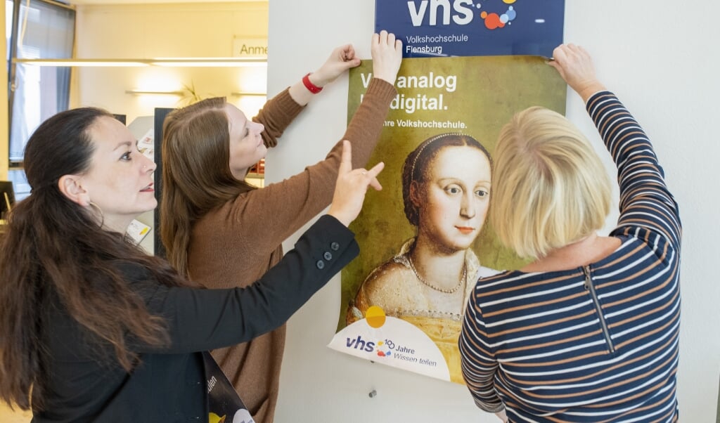 Sidste år fejrede VHS i Flensborg 100-års jubilæum, som pædagogisk leder Djenina Mortensen (til venstre) her sammen med kollegaer sætter plakater op for. Her var det digitale tilbud ikke det, som borgere møder i dag, et år senere. Arkivfoto: Tim Riediger (Tim Riediger / nordpool)