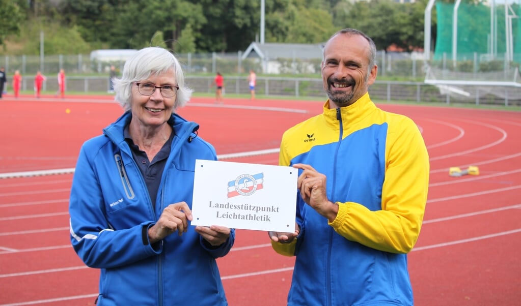 Kleines Schild mit großer Wirkung. Jan Dreier, 1. Vorsitzender des Kreisleichtathletikverbandes Flensburg (r.), freute sich über die Ernennung Flensburgs zum Landesstützpunkt durch Ursel Ahnfeldt, Vizepräsidentin des Schleswig-Holsteinischen Leichtathletikverbandes. Privat (Privat)