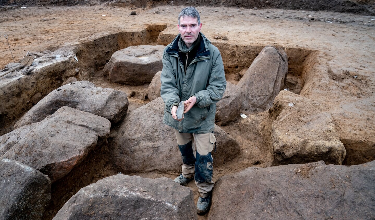 Ringo Klooß, Grabungsleiter, zeigt in der Ausgrabungsstelle eines Großsteingrabes aus der Trichterbecherzeit ein darin gefundenes Feuersteinbeil. Das auf einem schleswig-holsteinischen Acker gefundene Grab ist circa 5000 Jahre alt. Foto: 