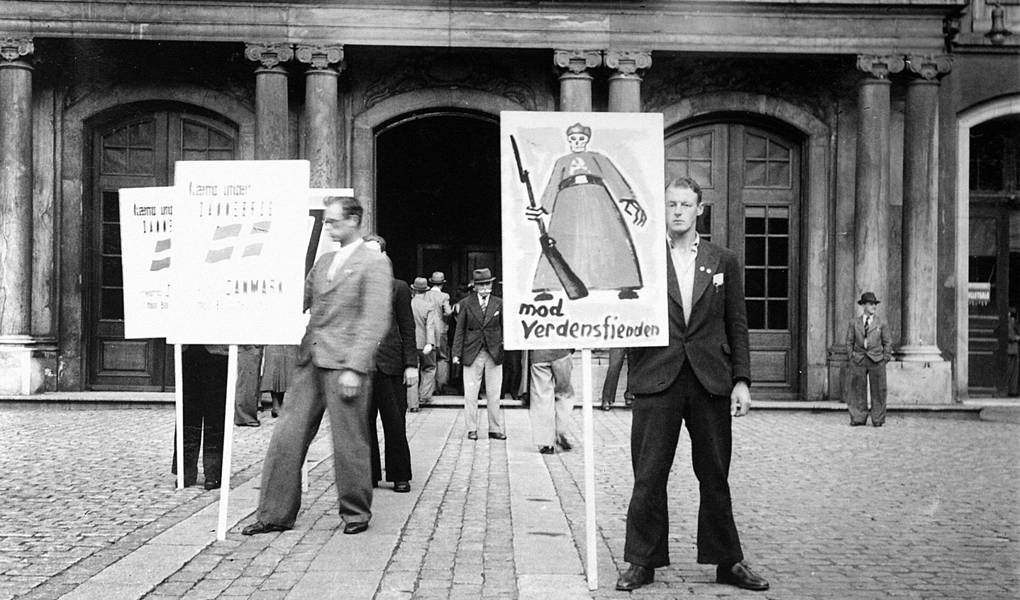 Danske nazister med hverveplakater for Frikorps Danmark foran Odd Fellow Palæet i København. Hans Hertel forsøger i et essay som et ordentligt menneske at forstå, hvordan ondskaben og stupiditeten kunne nå så ufattelige højder ved fronterne og i koncentrationslejrene. Foto: