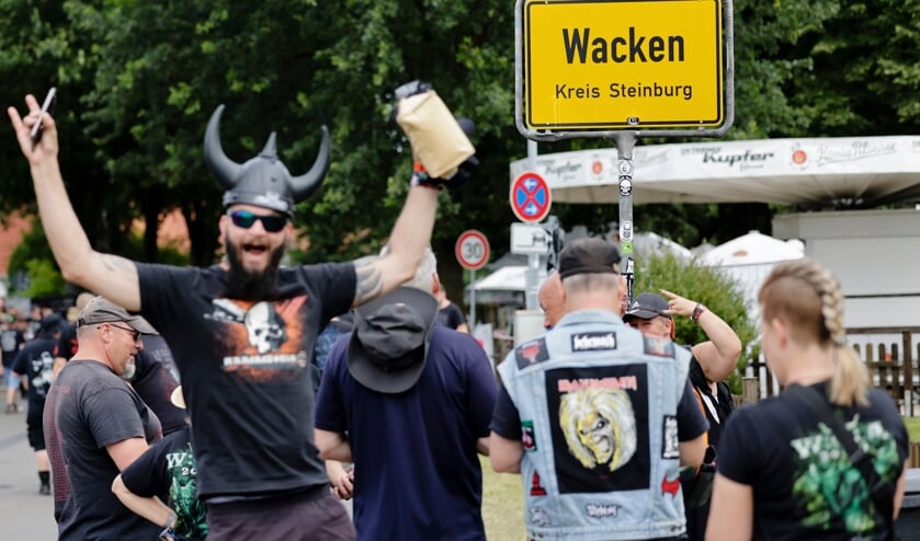 Ein Festival-Besucher posieren vor dem Ortseingangsschild in Wacken.