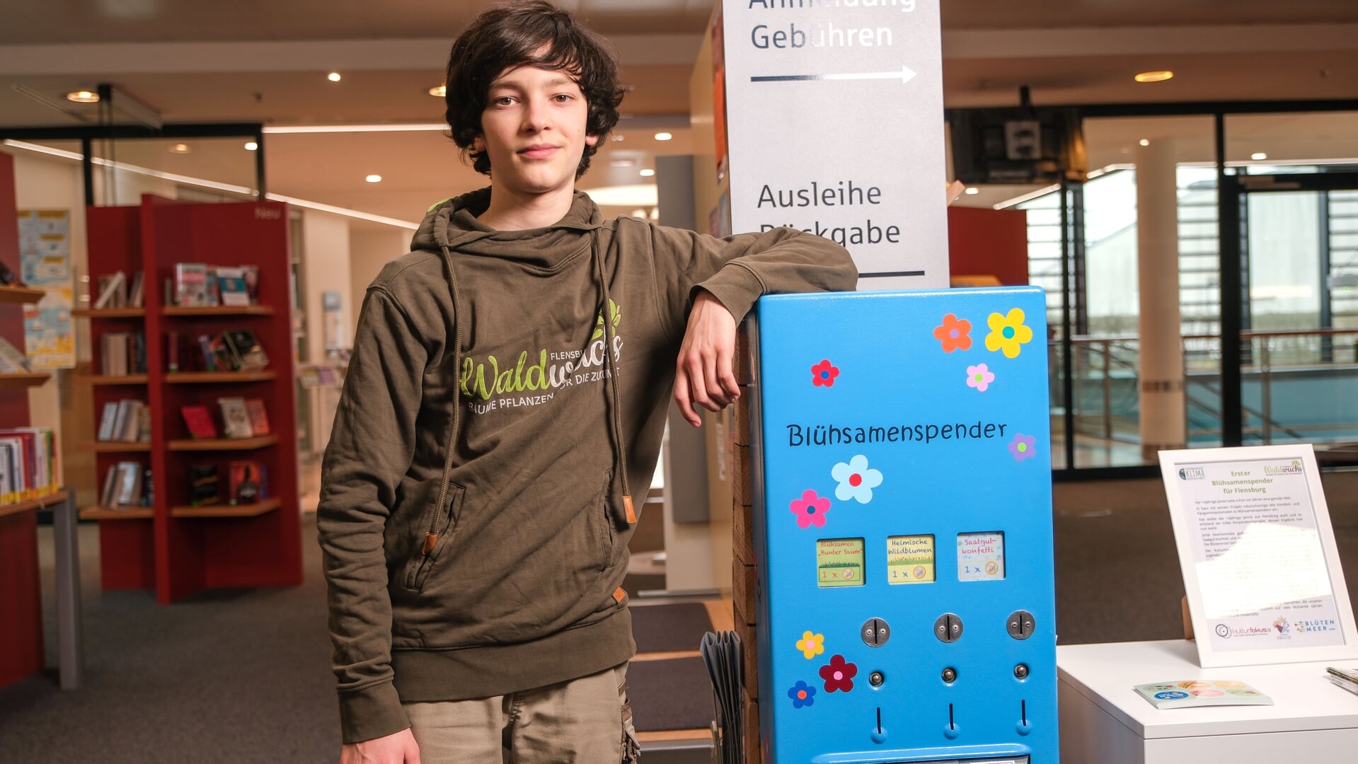 Der 14-jährige Jannis Ide präsentiert den Blühsamenspender, der aus einem alten Kondomautomaten gebaut wurde. In den nächsten Wochen steht der Saatgutautomat in der Flensburger Stadtbibliothek. Foto: