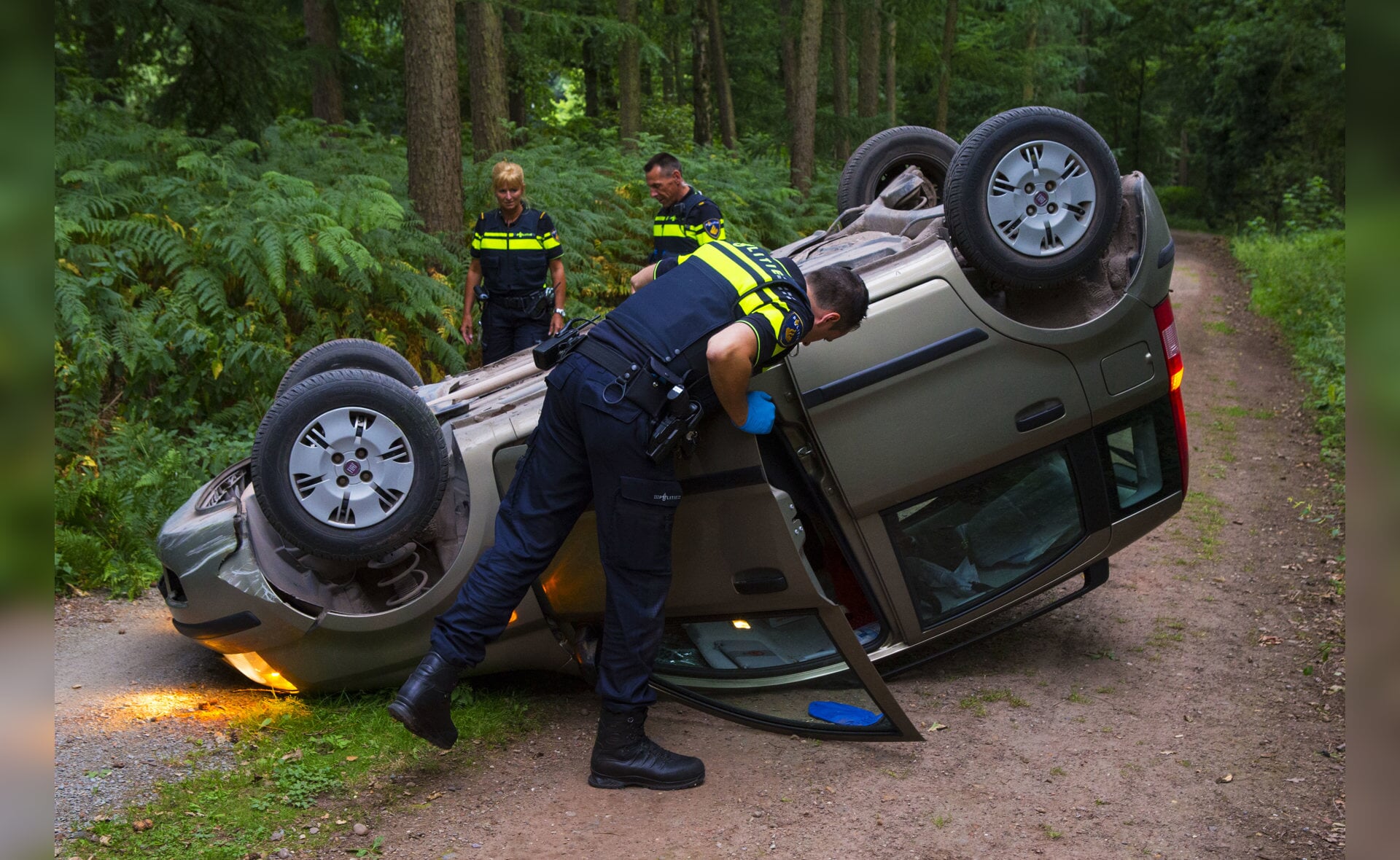 Een politieagent controleert de auto, die op de Heult botste tegen een paaltje en over de kop sloeg. (Foto: Sander van Gils).