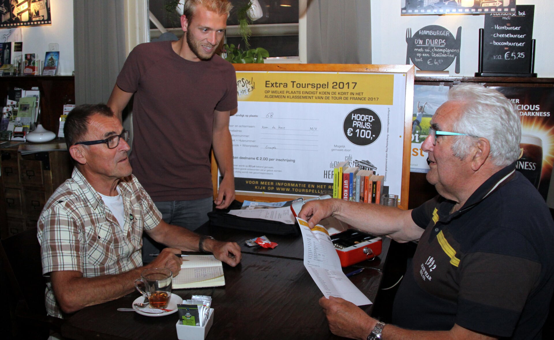 Roel van Lokven was donderdag een van de eersten die zijn inschrijfformulier inleverde voor het Tourspel Liempde. Vrijwilligers Jan van der Heijden (links) en Piet van Berkel bemanden de kassa. (Foto: Gerard Schalkx).