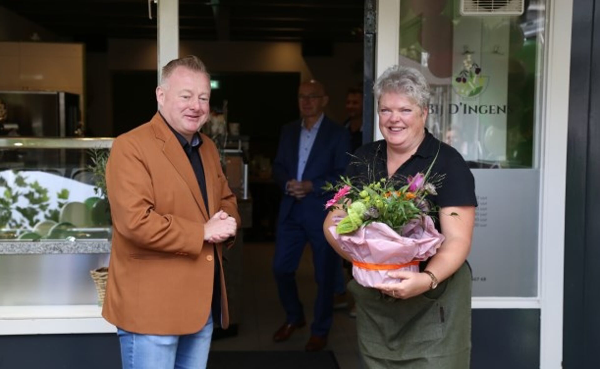 Ingrid van Veen neemt uit handen van wethouder Eric van den Broek een felicitatiegeschenk in ontvangst bij de opening van haar nieuwe zaak aan de Markt in Boxtel.