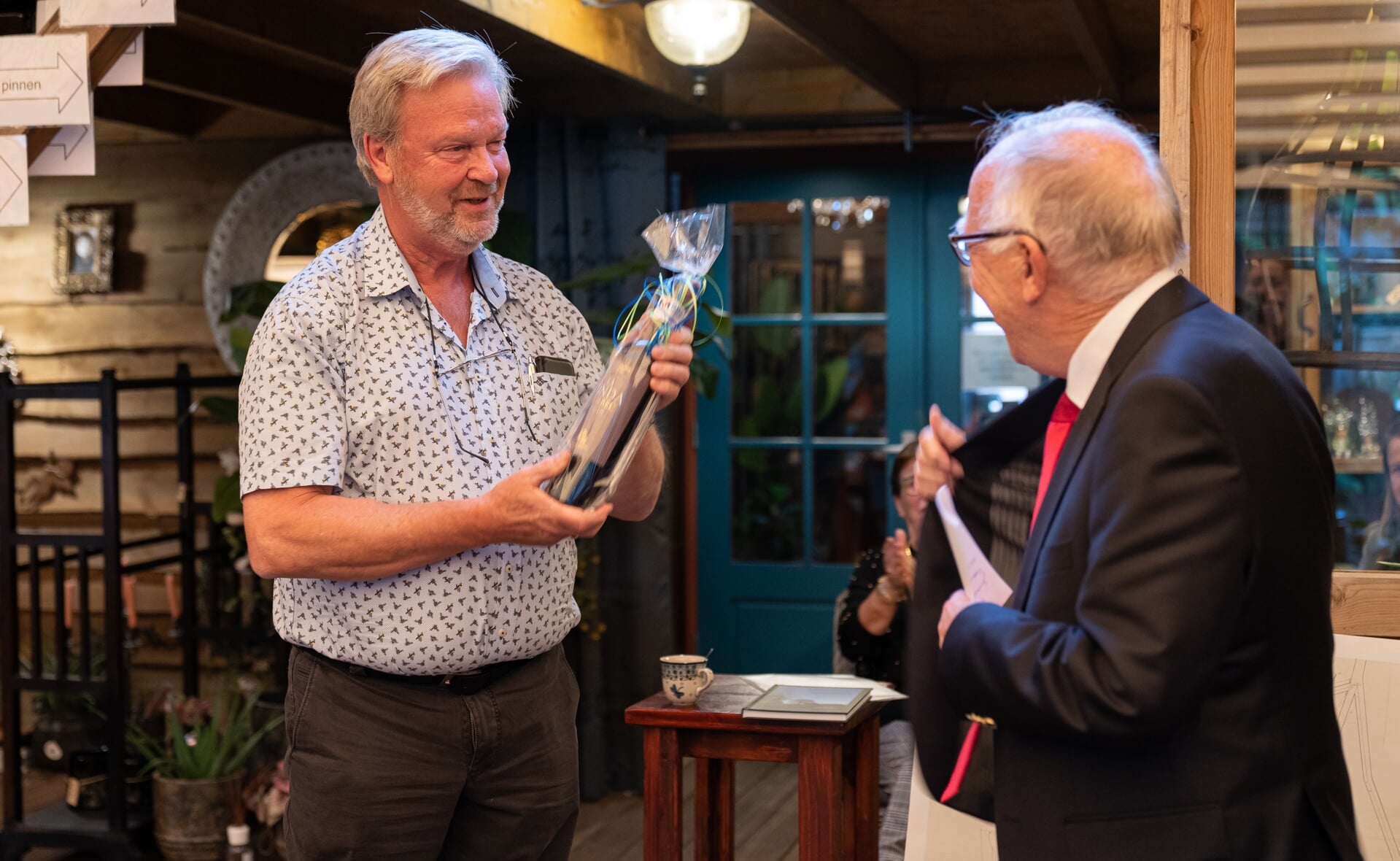 Henk Renders (links) kreeg een flesje wijn van Maarten Roelofs Heyrmans die op zijn beurt weer het eerste boek in ontvangst nam. (Foto: Daisy Renders).