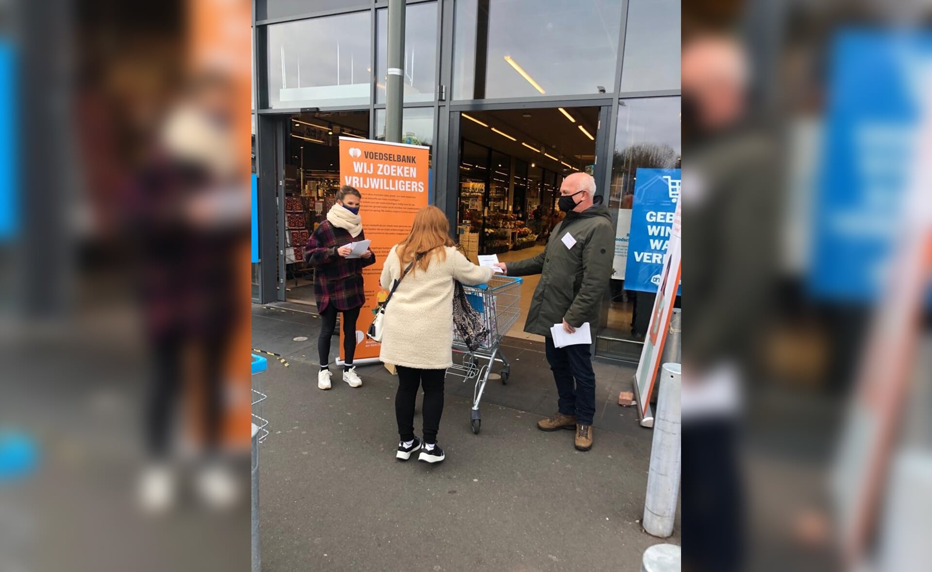 Vrijwilligers van de Voedselbank flyeren bij de deur van supermarkt Albert Heijn. Ze vroegen klanten om extra spullen te kopen. (Foto: eigen collectie). 