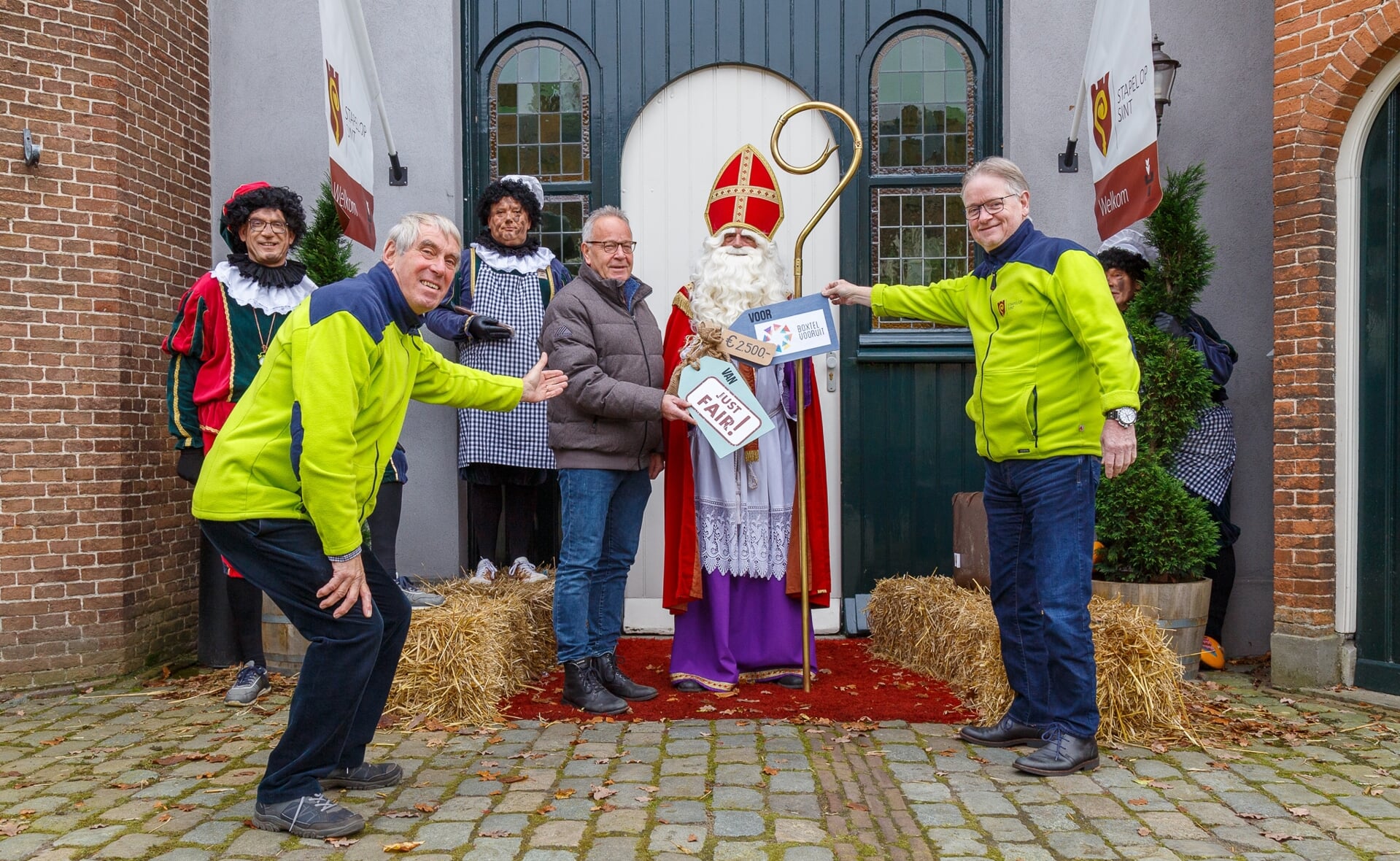 Onder toeziend oog van Sint-Nicolaas reikt Frank Geurtz van de opgeheven Wereldwinkel Just Fair een cheque van 2.500 euro uit aan voorzitter Wim Ketelaars (links) en secretaris Jan Staats (rechts) van Boxtel Vooruit. 