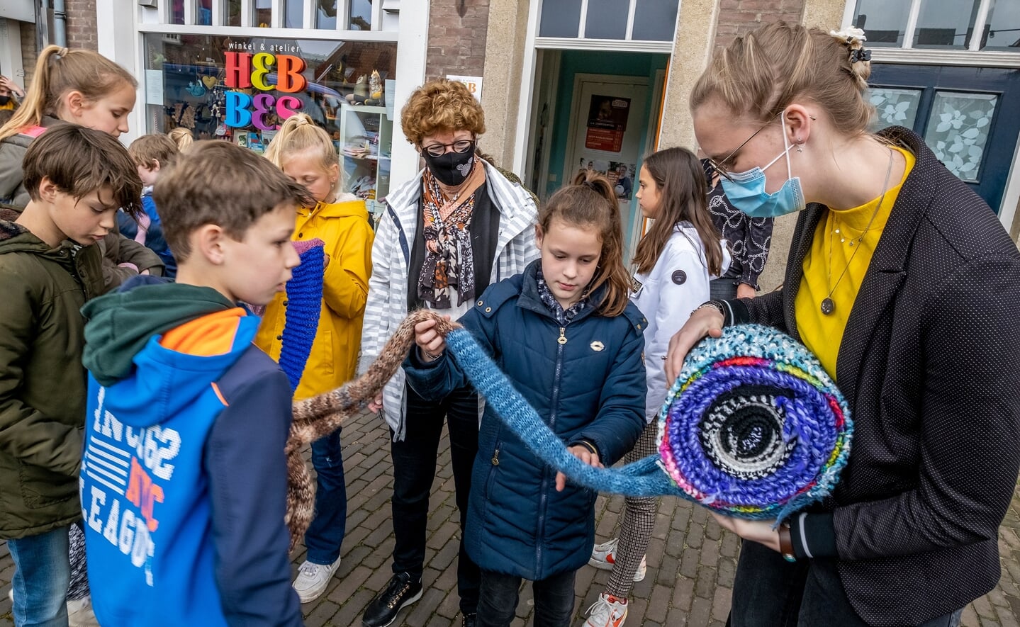 Medewerkster Minke van cadeauwinkel Hebbes aan de Markt (rechts) neemt de reuzensjaal van basisschool De Hobbendonken in ontvangst. Bij het oprollen van de sjaal wordt ze geholpen door leerkracht Gerry van Zanten (midden) en enkele leerlingen. (Foto: Peter de Koning). 