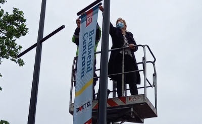 <p>Wethouder Mariëlle van Alphen bevestigt de eerste banier aan de mast. Bruisend Centrum Boxtel is nu nog zichtbaarder. (Foto: Jan Hermens)</p>