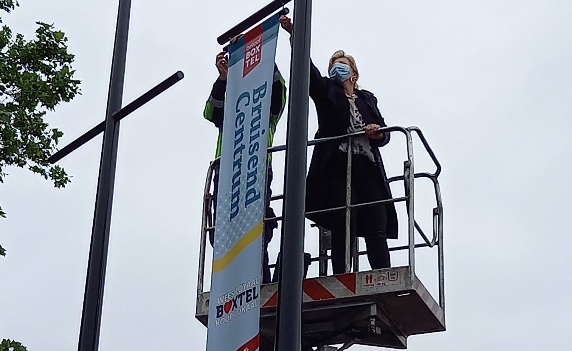 Wethouder Mariëlle van Alphen bevestigt de eerste banier aan de mast. Bruisend Centrum Boxtel is nu nog zichtbaarder. (Foto: Jan Hermens)