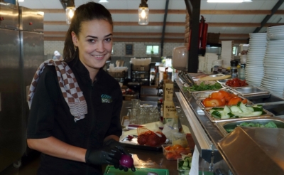 <p>Fenna Maas snijdt uien, komkommers en tomaten in de keuken van speelboerderij Gouden Woud. De Liempdse heeft het prima naar haar zin op haar werk. (Foto: Gerard Schalkx).</p>