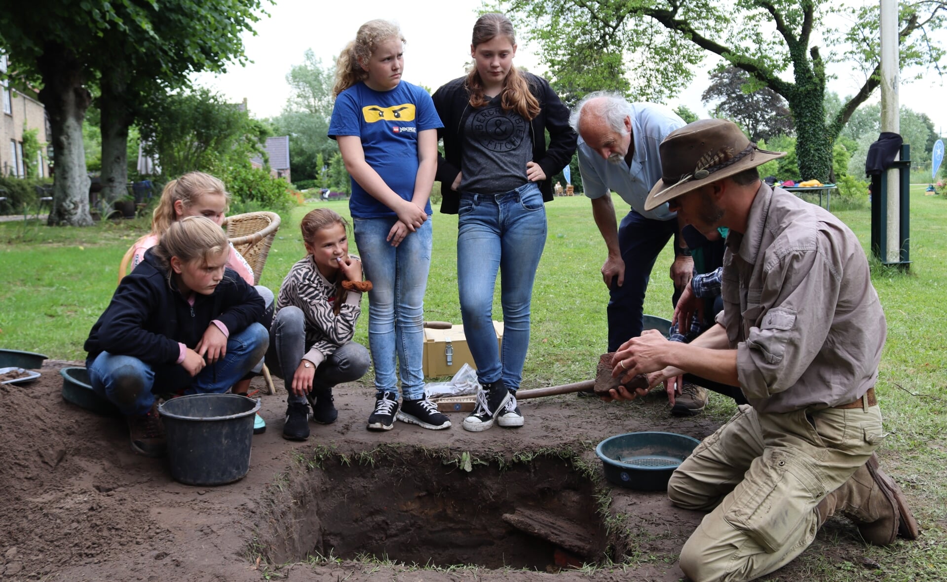 Archeoloog Johan Verspay (rechts) geeft uitleg bij de opgravingen in de tuin van de familie Plantema aan de Baarschot in Esch. Leerlingen van groep 7 en 8 speurden vorige week naar restanten van een kasteel dat hier ooit heeft gestaan. 