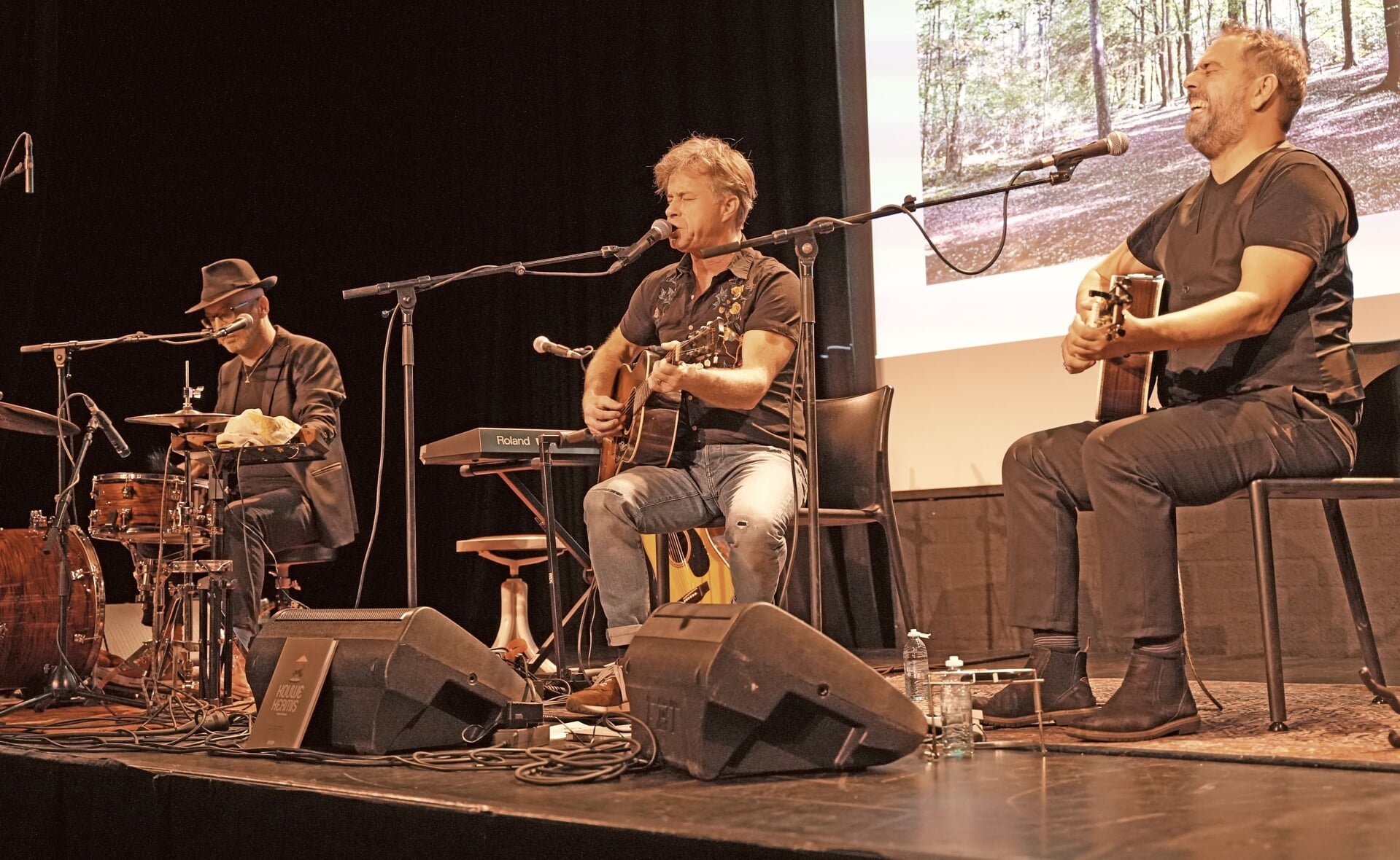 Singer-songwriter JW Roy zingt ‘Kouwe Kermis’ in Podium Boxtel. Links drummer en multi-instrumentalist Gabriël Peeters, rechts gitarist en boezemvriend Ruud van den Boogaard.