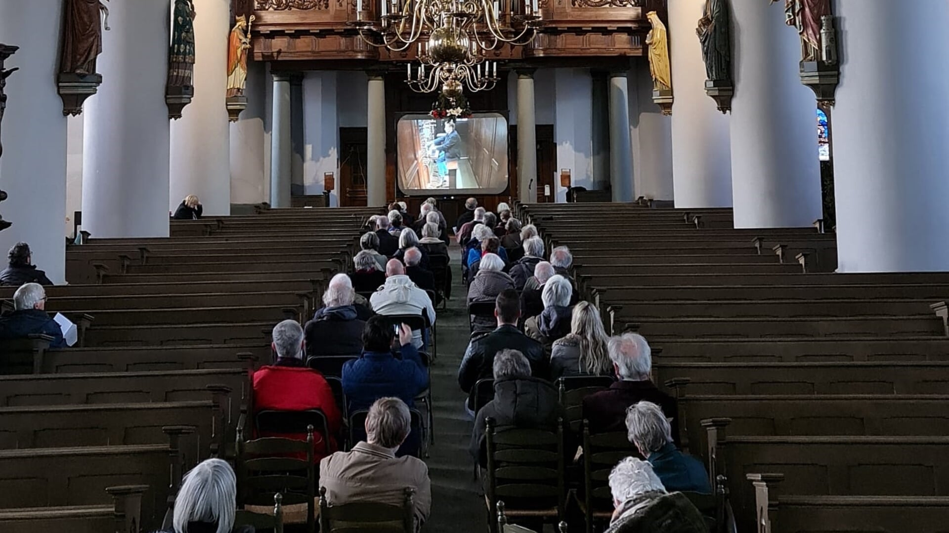 Meer dan vijftig luisteraars volgen de verrichtingen van Tommy van Doorn met hun oren en ogen. De organist is namelijk op een videoscherm te zien.
