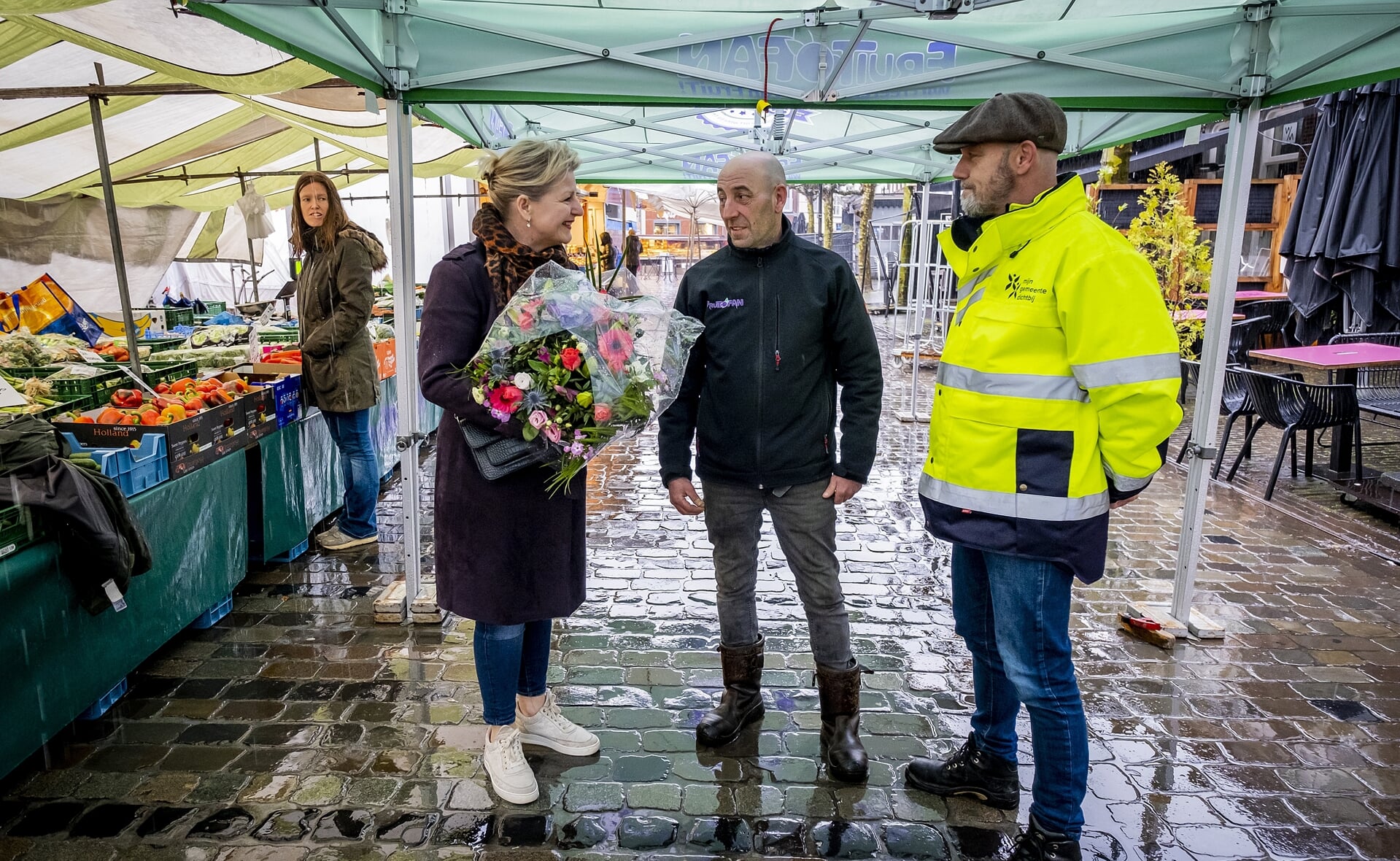 Jan-Maarten Platenburg stopt met zijn groente- en fruithandel op de Boxtelse weekmarkt. Wethouder Mariëlle van Alphen luidde hem uit met bloemen. Rechts marktmeester Richard Schuurs.