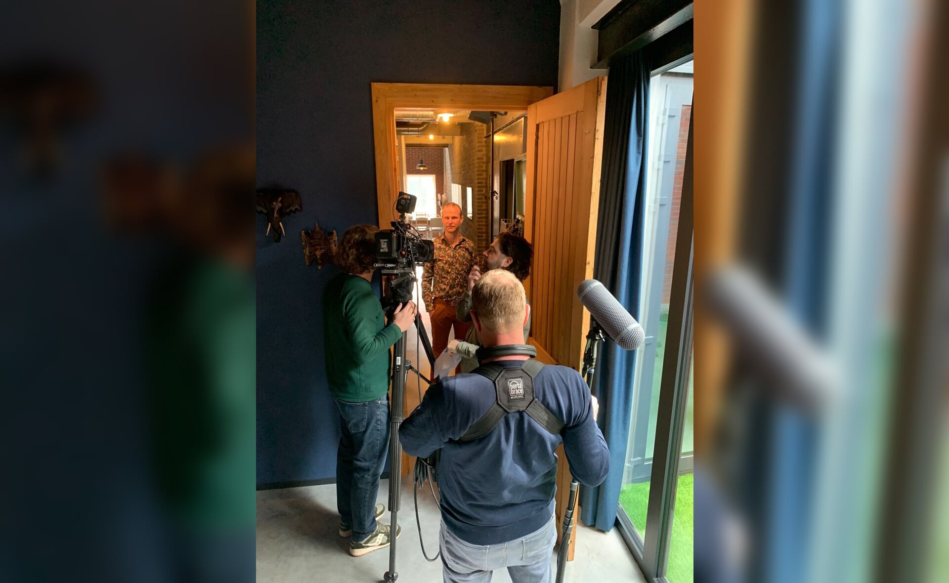 Mart Renders staat in de deuropening terwijl een filmploeg opnames van hem maakt.
