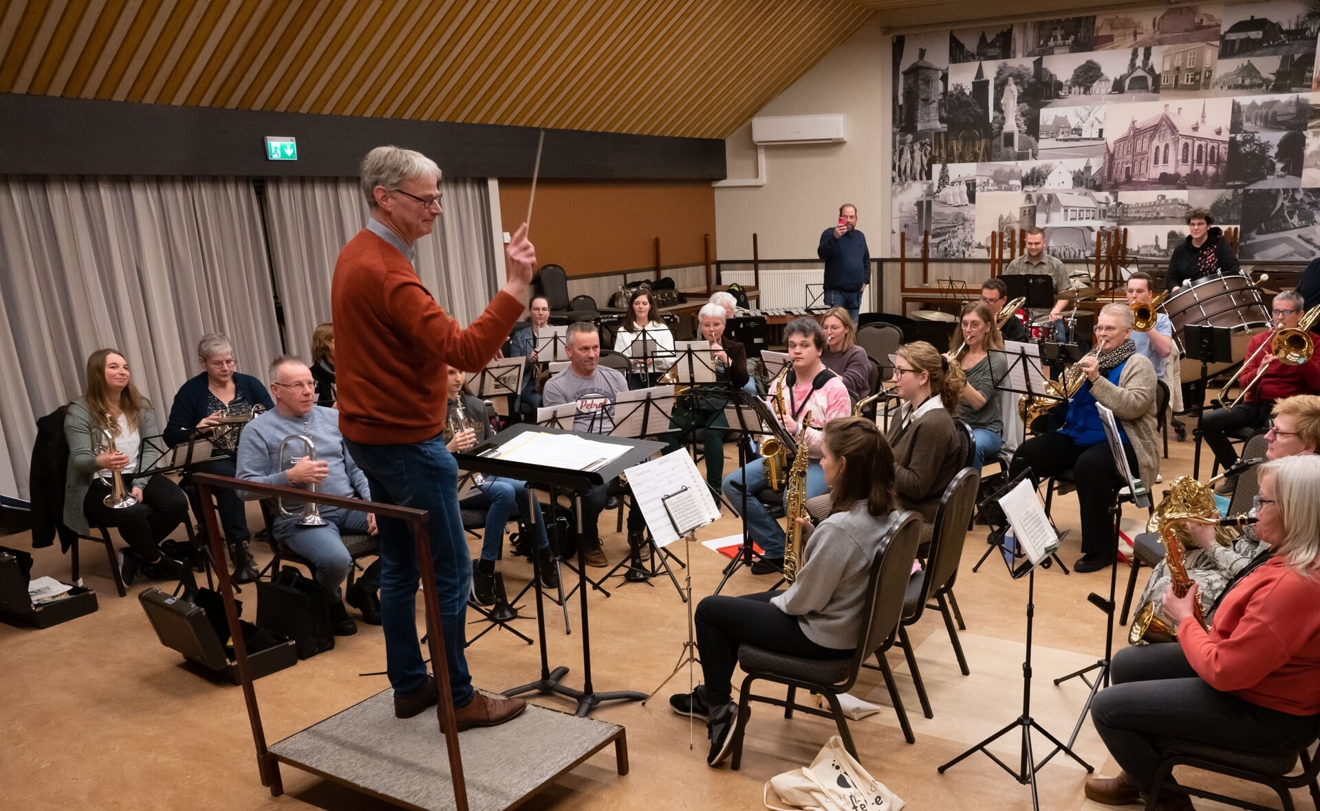 Hans van Bussel oefent zijn muziekstuk met orkest. Zijn concurrent Rick van de Ven staat achterin alvast foto's en filmpjes te maken, waarschijnlijk voor de technische analyse...