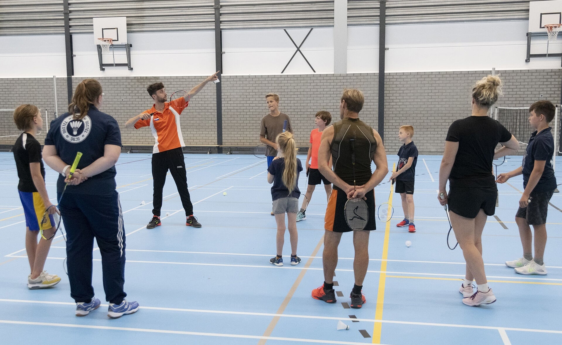 Het lijkt of Jacco Arends Usain Bolt nadoet, maar dat is niet zo. Hij geeft uitleg over badmintontechniek. Jeugdtrainers en kinderen luisteren naar zijn instructie.