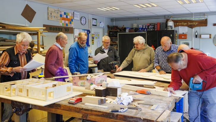 De mannen van de hobbyclub in het noodlokaal achter de Sint-Willibrordusschool. Links werkt Fons van der Heijden aan de maquette van het nieuwe onderkomen.