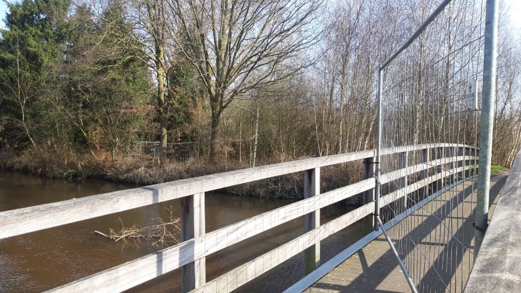 Een bouwhek is met kettingen en hangsloten aan de houten reling van de voetgangersbrug geklonken. (Foto: Henk van Weert). 
