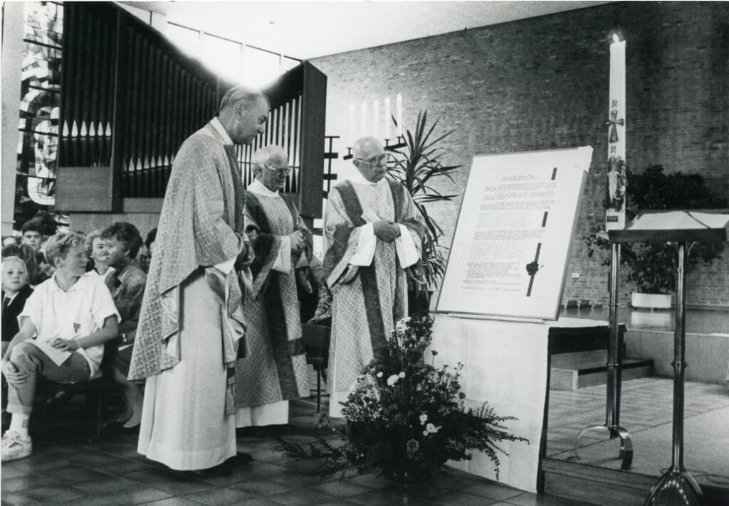 Pastoor Harry van den Tillaart bekijkt een oorkonde bij de plaatsing van glas-in-loodramen in de Maria Reginakerk. Links bisschop Jan Bluyssen, rechts emeritus pastoor Herman de Beer. (Foto: Piet van Oers, 1989).