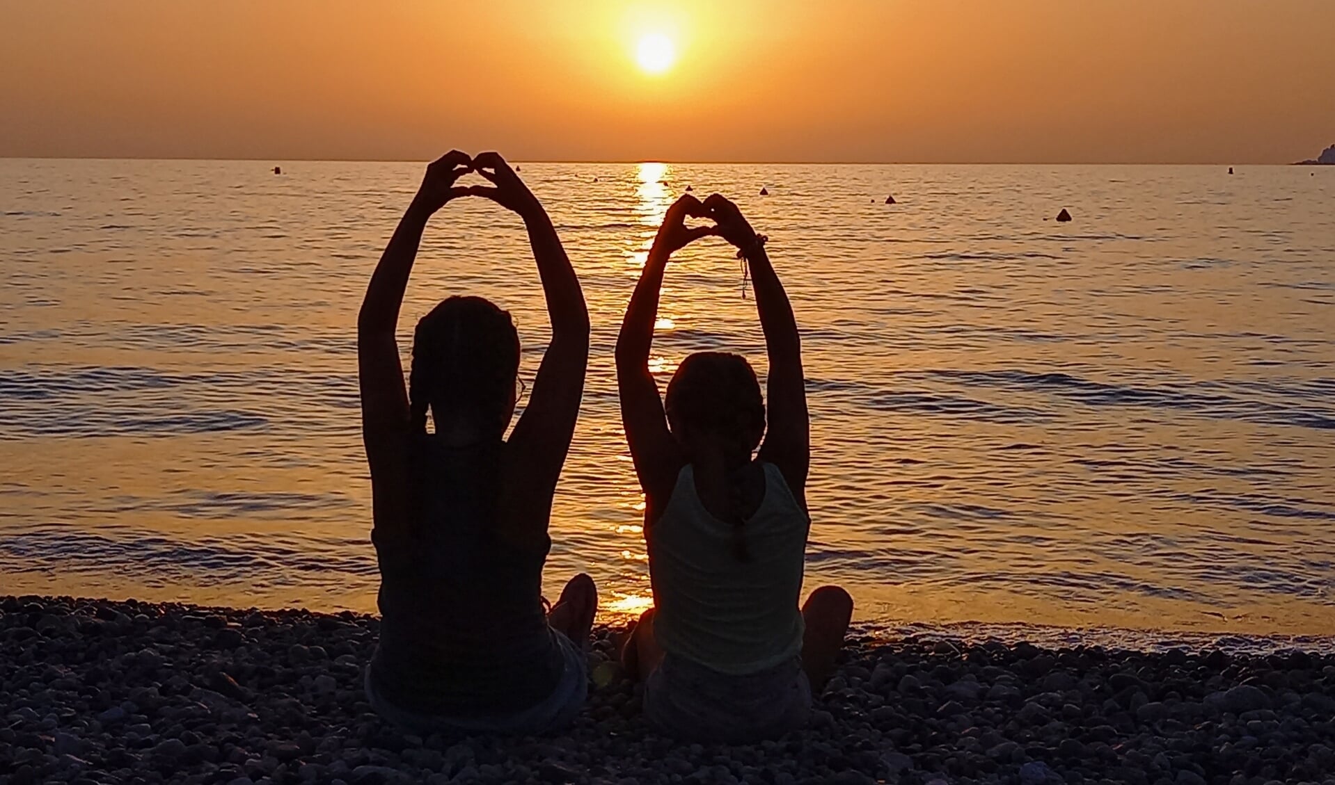 Onze 2 dochters die allebei een hartje maken met hun handen bij een zonsondergang aan het strand op het mooie eiland Corsica. 
