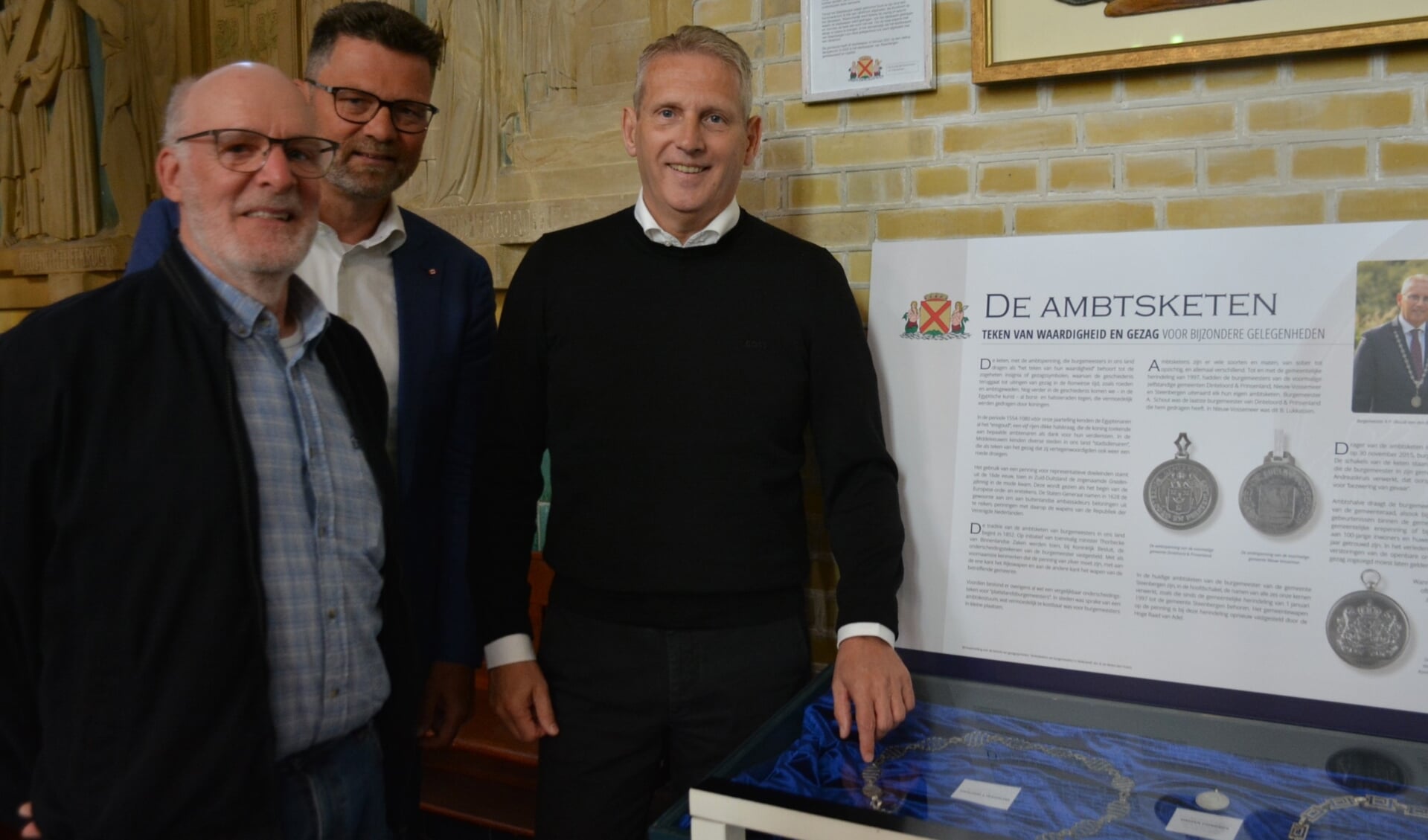 Sjaak Jasperse, Robert Catsburg en burgemeester Ruud van den Belt poseren trotst bij de vitrine met  ambtskettingen en -penningen die sinds zaterdag in het Vestinghuys in de Gummaruskerk is te bewonderen  