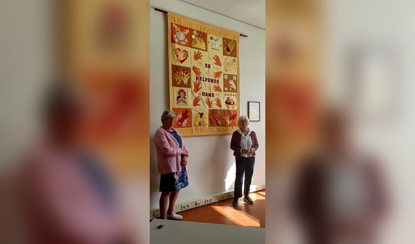 Annelies Groenewegen (links) en Thea Messemaker (rechts) voor het nieuwe wandkleed De Helpende Hand.