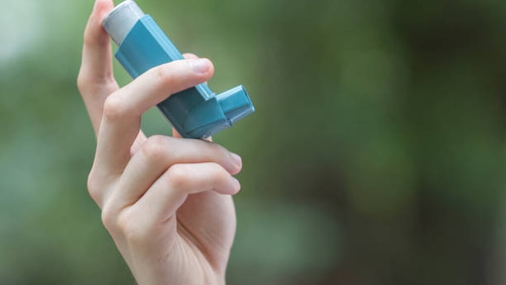 View of a man's hand holding a blue asthma inhaler