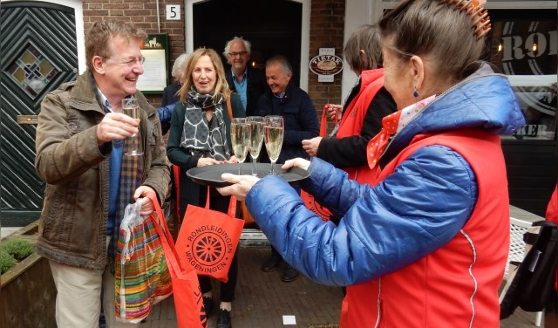 Louis Bouten met familie krijgt een glaasje Prosecco aangeboden als 40.000e deelnemer van Rondleidingen Wageningen.