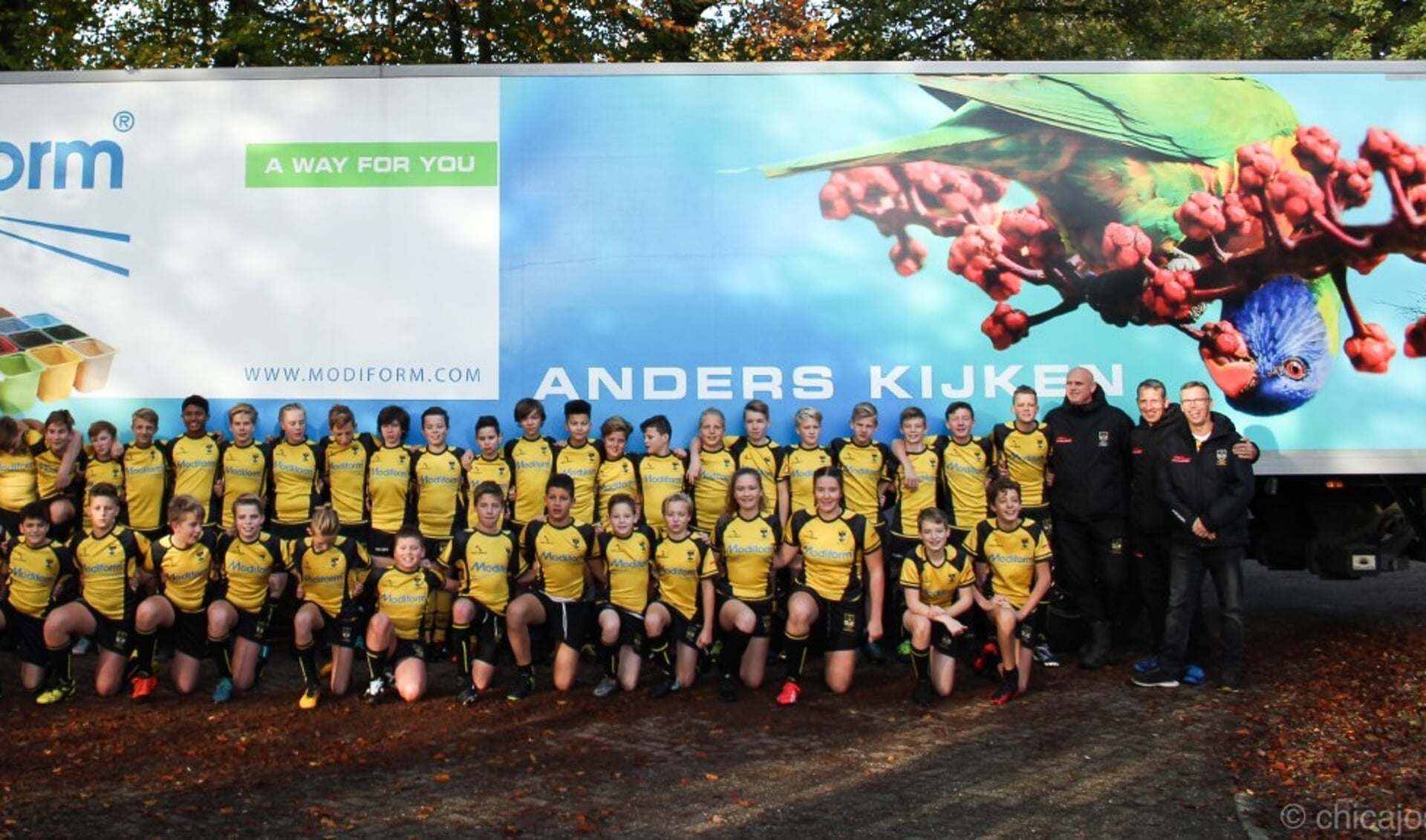 De rugbyjeugd en hun trainers voor een vrachtwagen van sponsor Modiform.