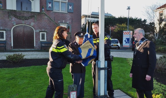 Oud-adjudant van de politie Wim Jansen hijst samen met wijkagent Leroy Vrijhoef de vlag bij het gemeentehuis.