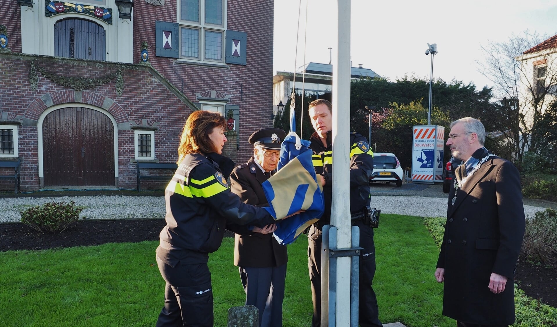 Oud-adjudant van de politie Wim Jansen hijst samen met wijkagent Leroy Vrijhoef de vlag bij het gemeentehuis.