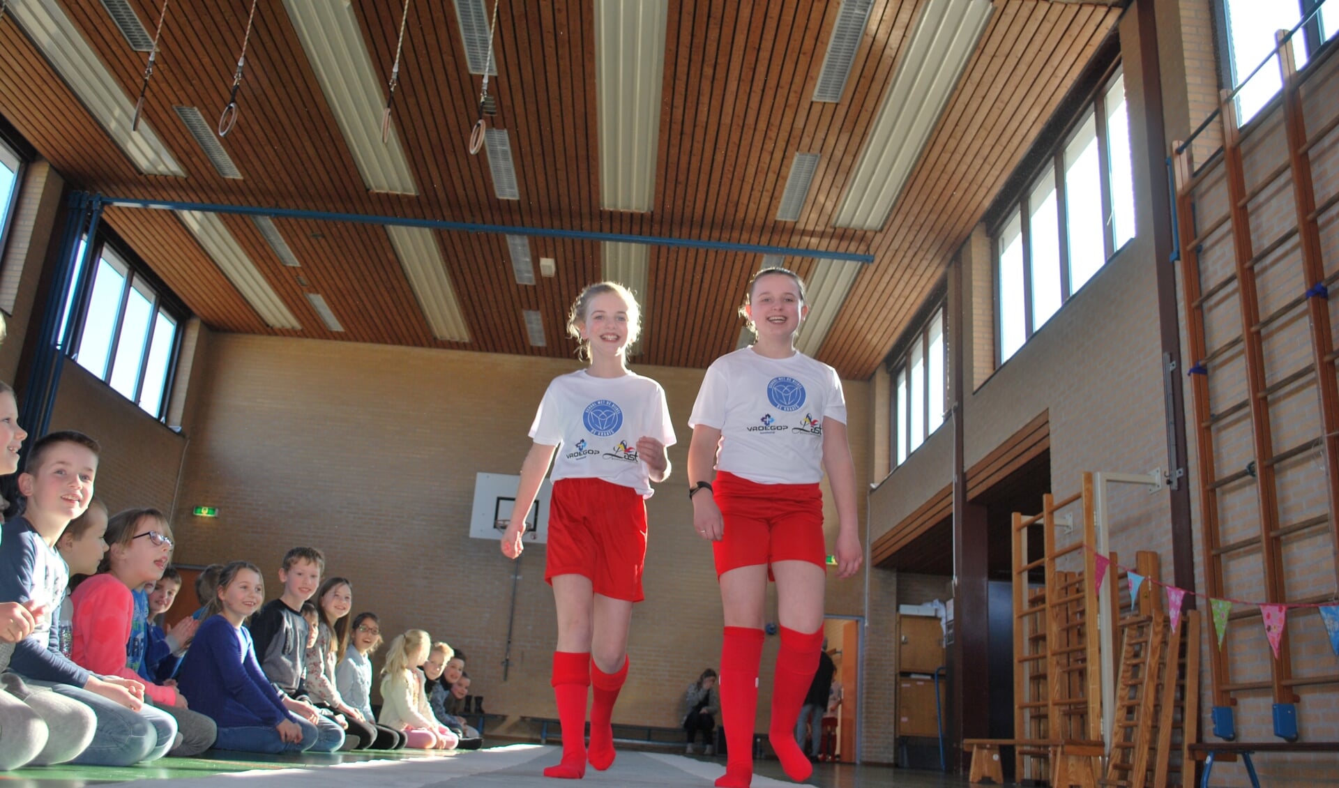 Marinke Moesker (links) en Hannah van Helden uit groep 7 showen op de lange mat in de gymzaal de mooie, nieuwe sportkleding van de Kraatsschool