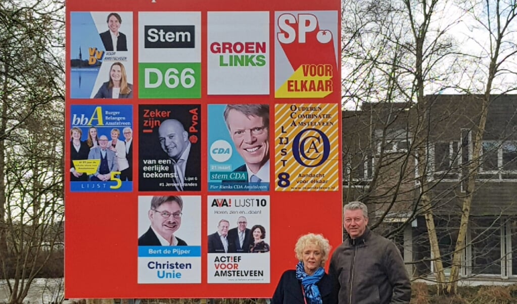 Jeannette van Heijningen en Mario van Deijzen bij een verkiezingsbord vol partijposters.