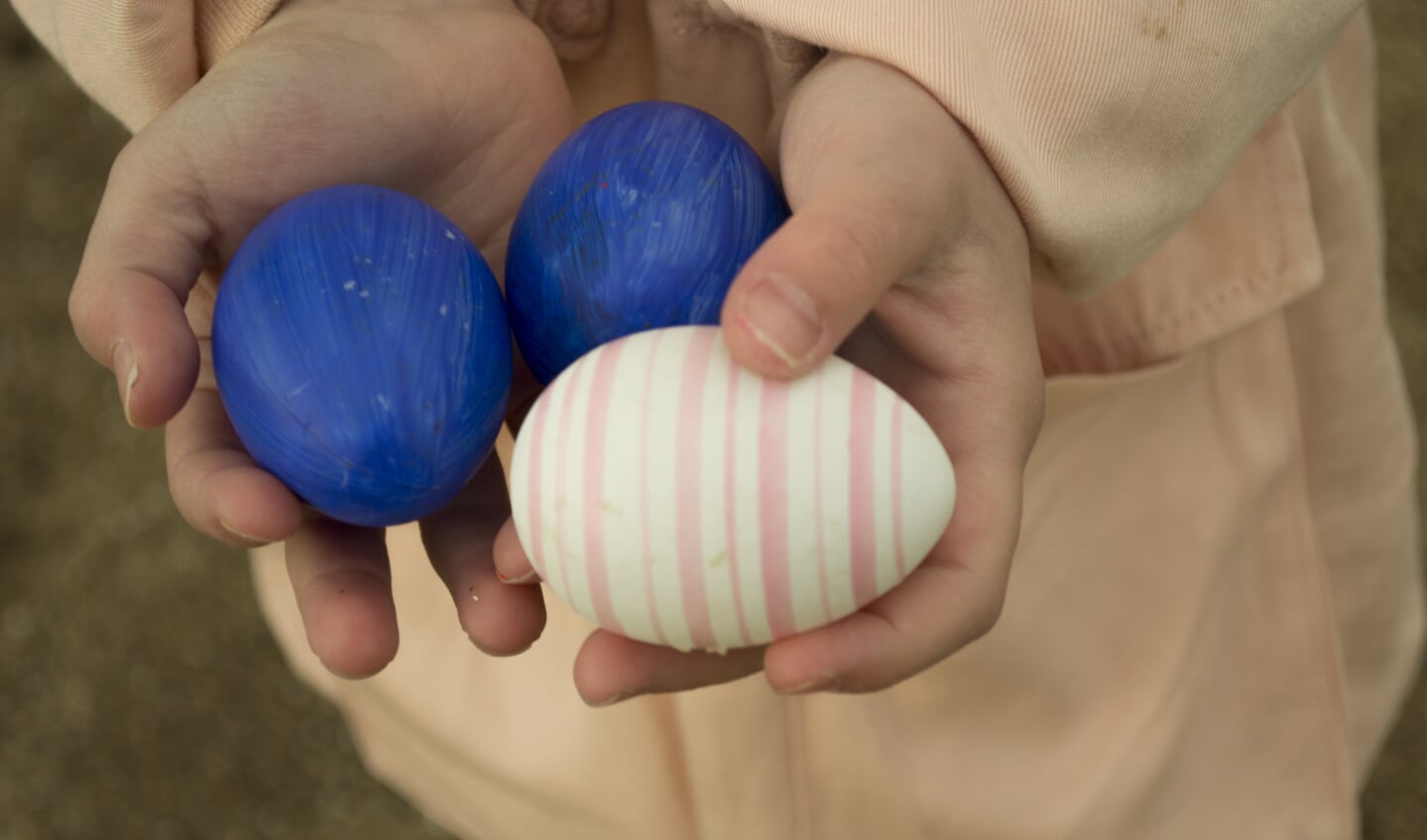 twee kinderhanden houden drie gekleurde eieren vast