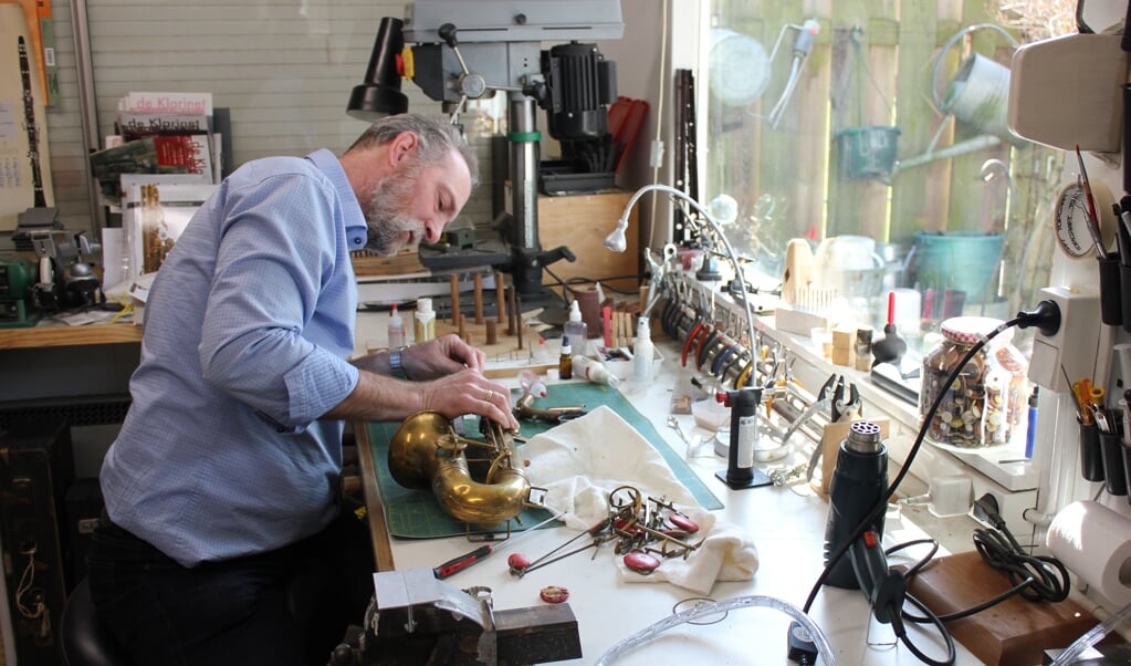 Edgar Lerk (50) buigt zich in zijn werkruimte over een te repareren saxofoon-in-delen.