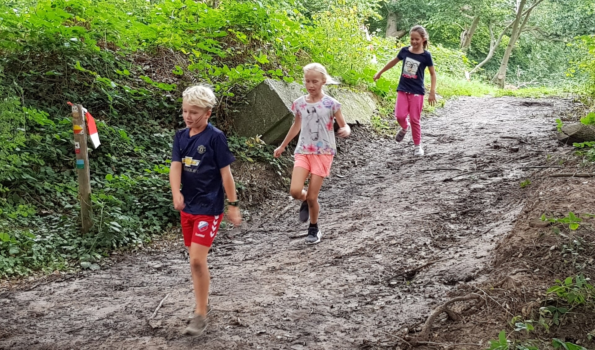Drie kinderen glibberen over de helling tijdens de Mud Vally Kids obstacle run.