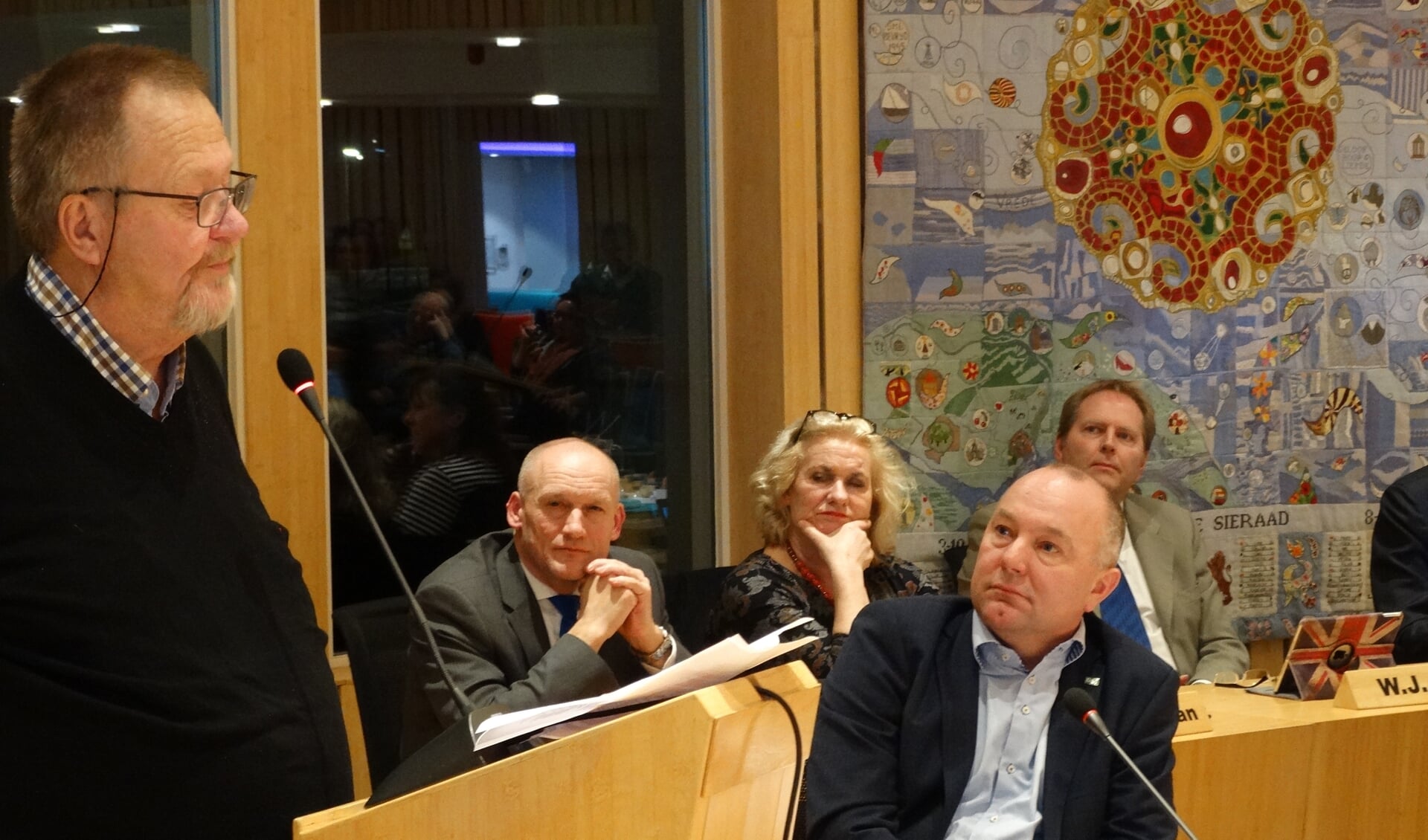 Jan Oechies (links) aan het woord, met rechts Bart van Aspert (D66) en op de achtergrond het college
