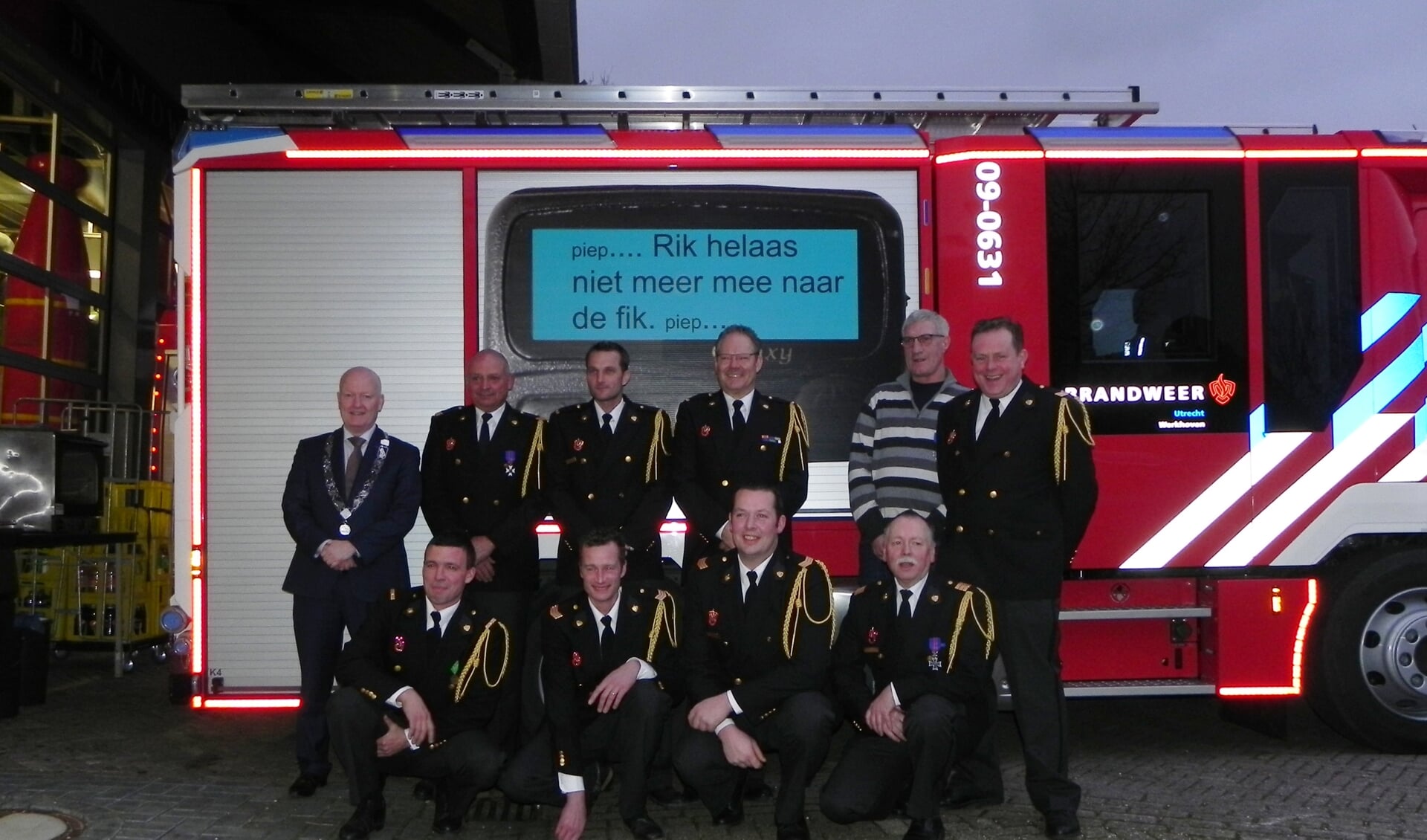 De negen geëerde brandweermannen poseren tezamen met burgemeester van Bennekom voor de nieuwe brandweerwagen.  