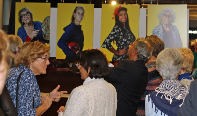 Bezoekers van de opening bekijken en bespreken de foto's van de heldinnen.