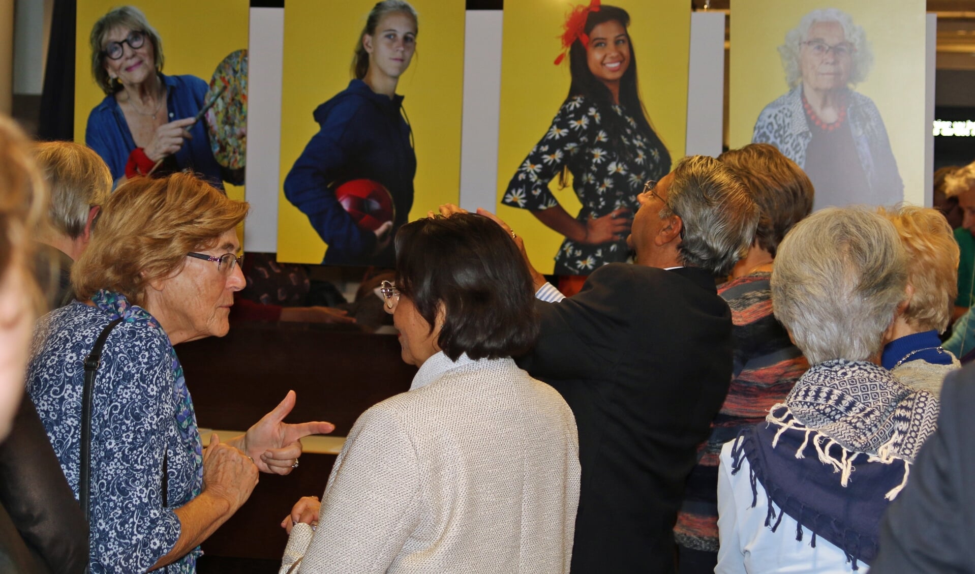 Bezoekers van de opening bekijken en bespreken de foto's van de heldinnen.